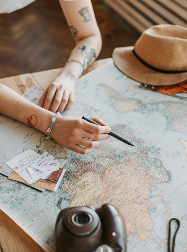 Tattooed woman planning a trip with a world map, passports, and travel essentials on a wooden table.